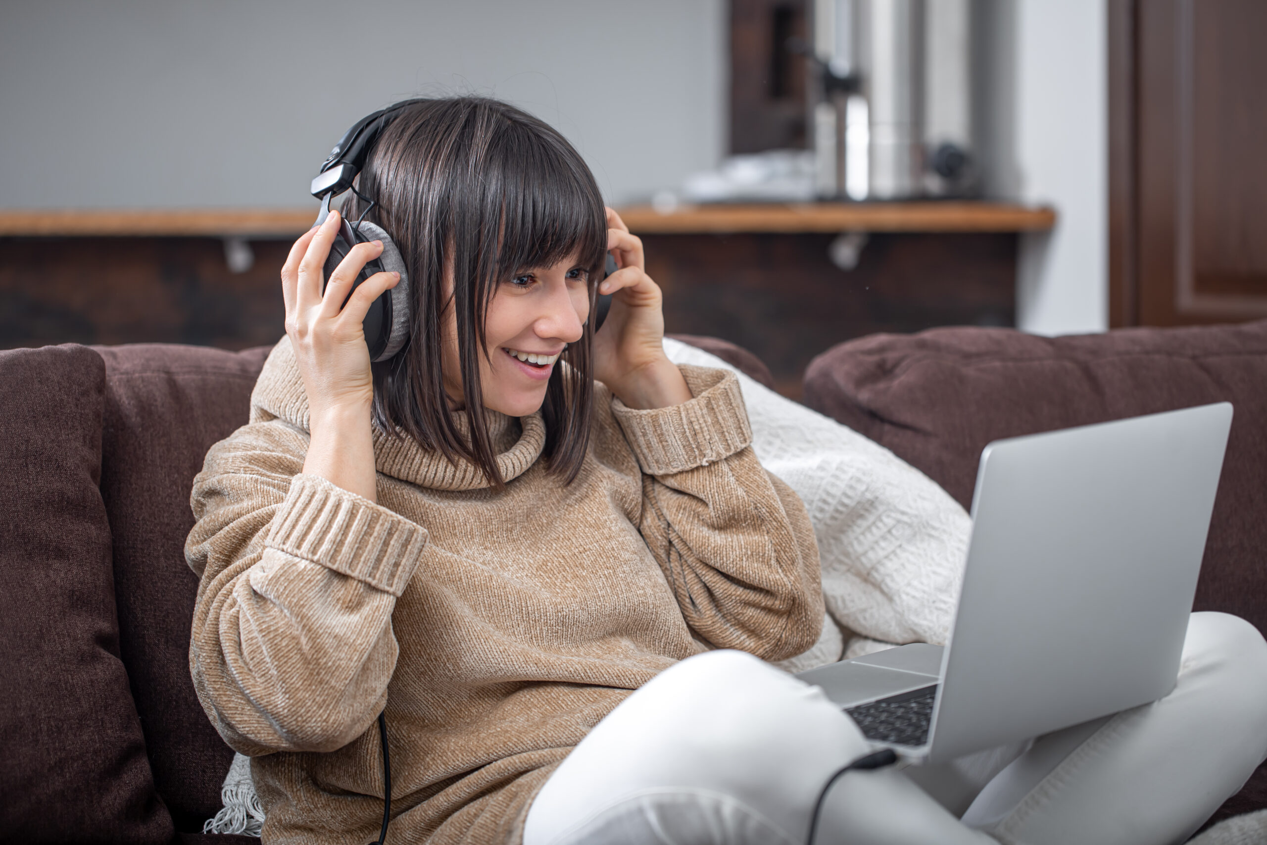 A beautiful smiling girl in headphones looks into the laptop screen.
