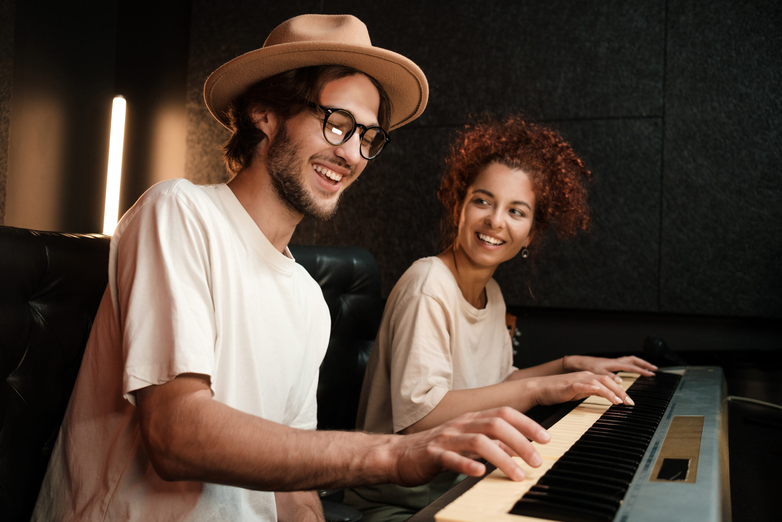 Young stylish musicians happily playing on piano keyboard record